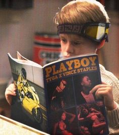 a young boy reading a book with goggles on his head