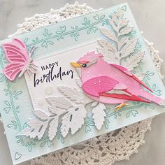 a birthday card with a pink bird and butterfly on it, sitting on a doily