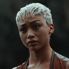 a close up of a person with short hair and piercings on her ears, wearing a brown top