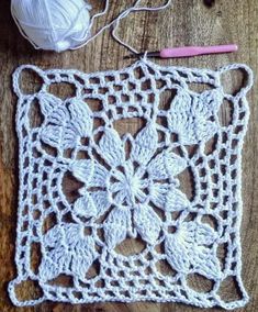 a crocheted doily sitting on top of a wooden table next to a ball of yarn