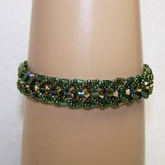 "A shiny green bracelet fit for a goddess. This piece was made using 3mm golden Swarovski bicone crystals surrounded with 3mm green iridescent glass squares and rainbow green seed beads. All together they are just beautiful. This is one of my favorite bracelets It will fit a 7.5\" wrist and measures just about 3/4\" wide. It fastens with a silver toggle clasp. If you love greens, you must have this bracelet." Elegant Green Beaded Bracelets With Tiny Beads, Green Emerald Bracelets For Party, Green Beaded Bangle Bracelets With Spacer Beads, Green Beaded Bangle With Spacer Beads, Green Faceted Beads Bangle Bracelet, Green Bangle Bracelet With Faceted Beads, Green Jubilee Bracelet Jewelry For Party, Green Beaded Bangle Crystal Bracelet, Green Beaded Crystal Bangle Bracelet