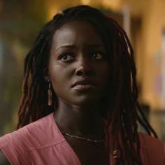 a woman with dreadlocks stares at the camera in a dimly lit room,