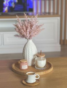 a white vase with some pink flowers in it on a tray next to a cup