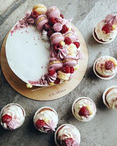 a cake with frosting and raspberries on top surrounded by cupcakes