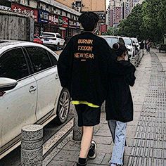 two people walking down the sidewalk in front of parked cars