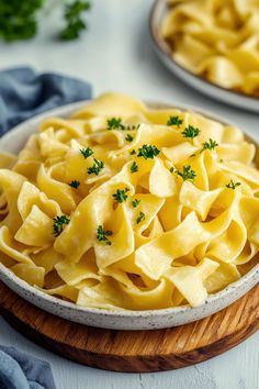 a bowl filled with pasta and parsley on top of a wooden board next to another plate