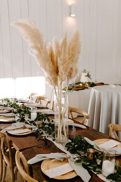 the table is set with place settings and flowers in tall vases on each side