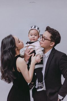 a man and woman holding a baby in front of a gray background with the caption's name on it