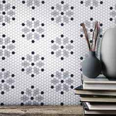 two vases sitting on top of books next to each other in front of a wall with hexagonal tiles