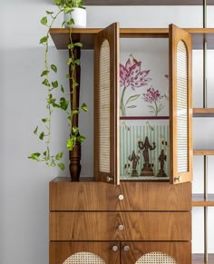 two chairs sit in front of a wooden cabinet with artwork on it and a potted plant