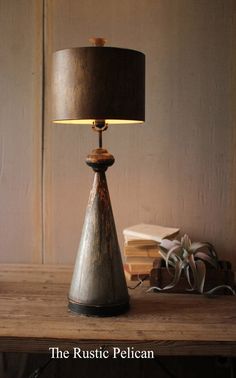 the rustic pelican table lamp has a black shade on it and is next to a stack of books