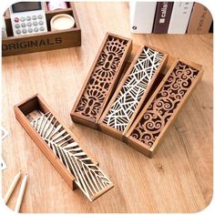 four wooden boxes with carved designs on them sitting on a table next to books and pencils