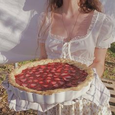 a woman holding up a pie with strawberries on it