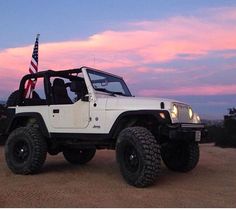 a white jeep with an american flag on the roof is parked in front of a pink sky