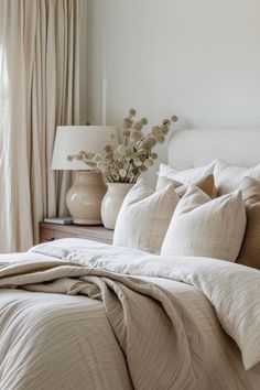 a bed with white sheets and pillows next to a lamp on a nightstand in front of a window