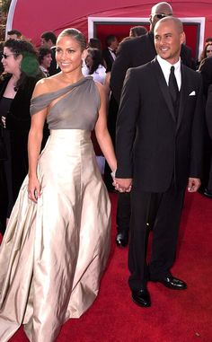 a man and woman in formal wear walking down a red carpeted area holding hands