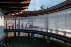 people walking across a bridge over water in front of a building with lots of windows