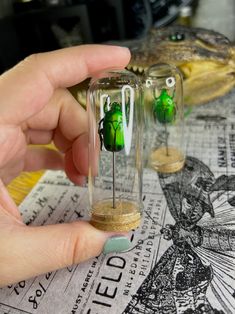 a person holding a tiny glass jar with some green things in it on top of a table