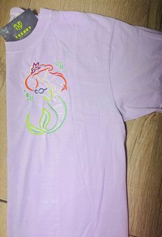 a t - shirt with an image of a little mermaid on it is laying on the floor