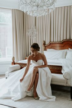 a woman sitting on top of a bed in a white dress next to a chandelier