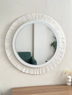 a white round mirror on the wall above a table with a green chair and potted plant