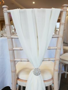 the back of a chair with a white cloth draped over it and a crystal brooch