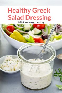 healthy greek salad dressing in a glass jar with a spoon and bowl of salad behind it