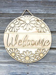 a welcome sign hanging on the side of a wooden wall with flowers and leaves around it