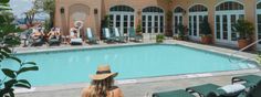 a woman sitting in front of a swimming pool with lounge chairs around it and people lounging on the patio