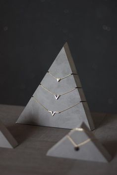 three small triangle necklaces sitting on top of each other in front of a pyramid