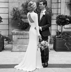 a man and woman standing next to each other in front of a building with potted plants