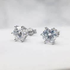 two pairs of diamond stud earrings on a white surface with the top one being cut in half