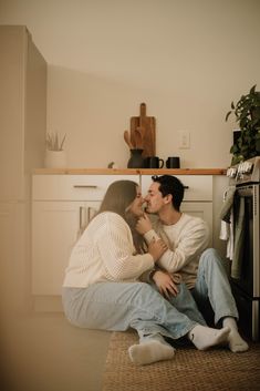 a man and woman sitting on the floor in front of an oven kissing each other