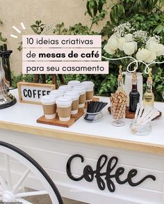 a table topped with coffee cups next to a white flower covered wall and greenery