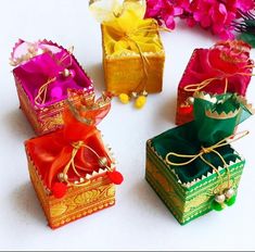 four colorful boxes with ribbons tied around them on a white surface next to pink and purple flowers