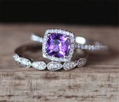 an engagement ring with a purple stone surrounded by white diamonds on top of a piece of wood