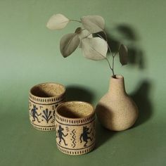 three vases with designs on them and a plant in the middle, against a green background