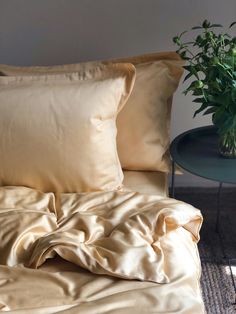 an unmade bed with two pillows and a potted plant on the end table