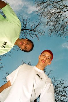 two men standing next to each other in front of a blue sky and tree with no leaves