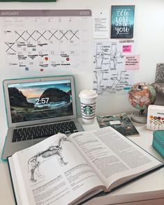 an open book sitting on top of a desk next to a laptop computer and coffee cup