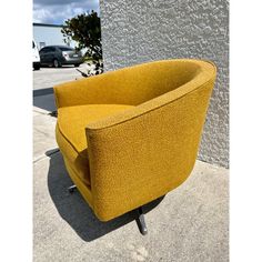 a yellow chair sitting on top of a cement floor next to a building with cars parked in the background