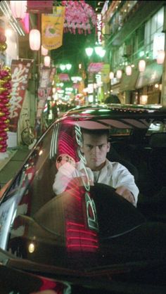 a man sitting in the driver's seat of a car on a city street at night