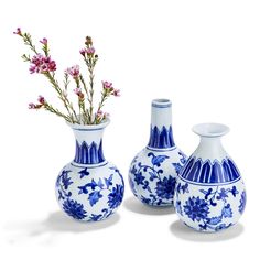 two blue and white vases with flowers in them on a white surface, one is empty