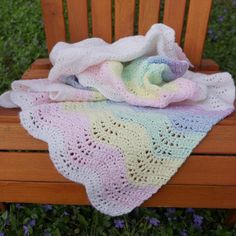 a crocheted blanket sitting on top of a wooden bench next to purple flowers