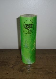 a green plastic cup sitting on top of a wooden table next to a white wall