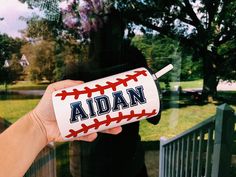 a person holding up a baseball bottle with the word adian on it in front of a fence