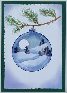 a blue ornament hanging from a tree branch with snow and pine trees in the background