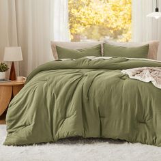 a bed with green sheets and pillows in front of a window