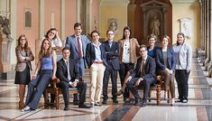 a group of people standing and sitting in front of a marble floored room with columns