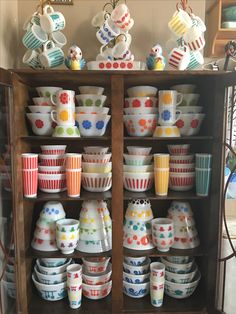 a cabinet filled with lots of colorful cups and saucers on top of wooden shelves